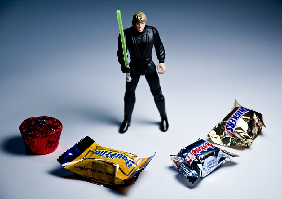luke skywalker action figure, behind, four, assorted-brand chocolate packs, temptation, fight, surrounded, overwhelmed, outnumbered, offense