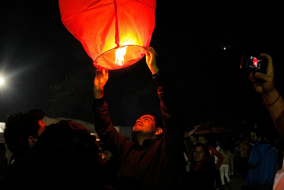 man, b lack jacket, holding, sky lantern, jacket, night, people, crowd, celebration, event