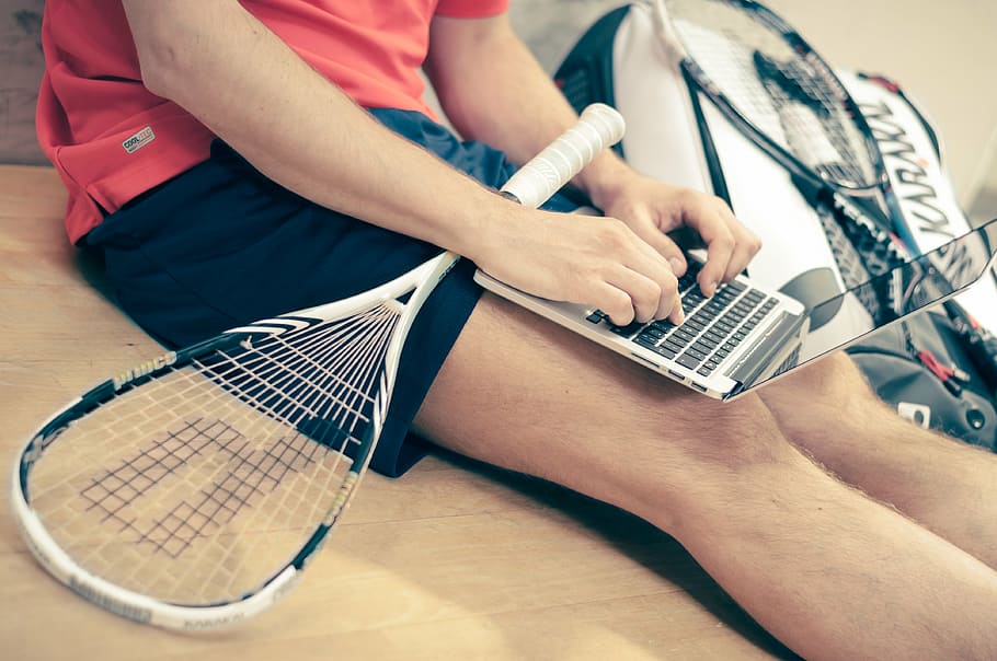 Hombre, usando, computadora portátil, al lado, raqueta de tenis, Macbook, aire, blanco, tenis, raqueta