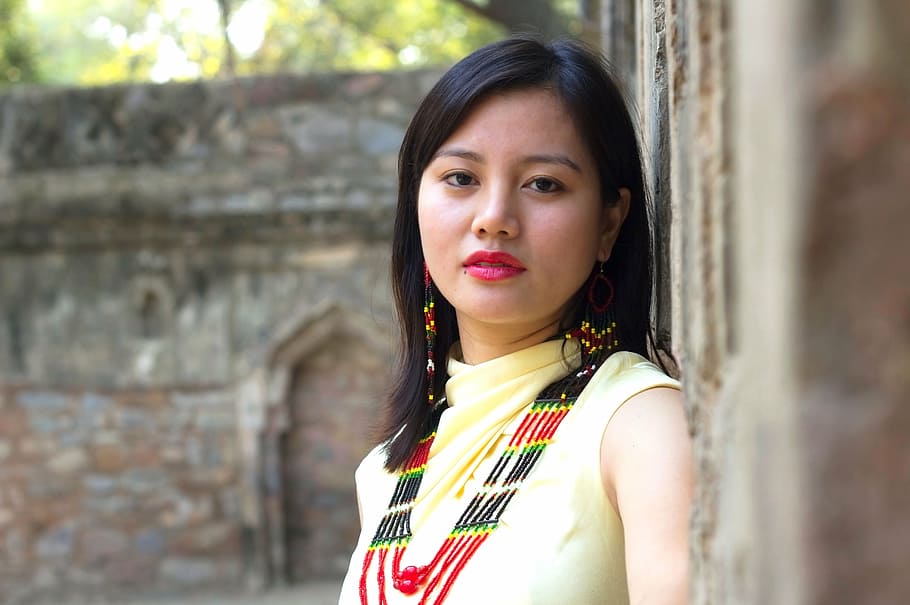 woman, wearing, yellow, shirt, leaning, brown, concrete, wall, daytime, tribal attire
