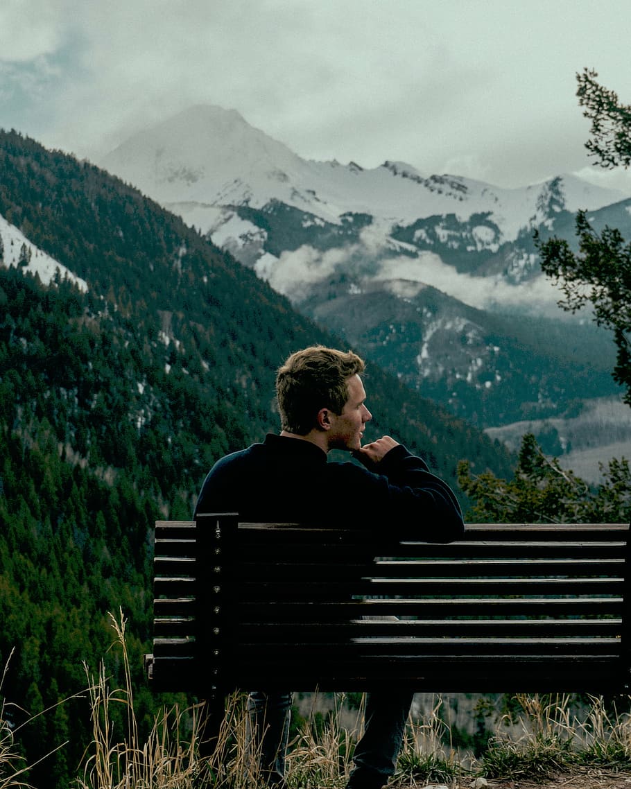 man, sitting, bench, front, mountain, daytime, mountains, trees, snow, smoke