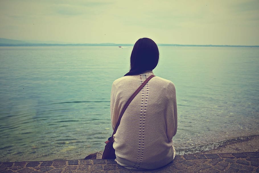 woman, sitting, brown, concrete, pavement, ocean, daytime, white, long, sleeve