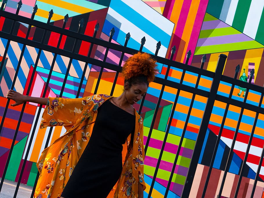 woman, wearing, black, boat-neck dress, leaning, fence, wall, art, public, colorful